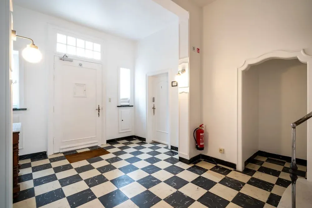 De inkomhal van The Rose Suites met zwart-wit geblokte vloer en de voordeur met bovenlicht